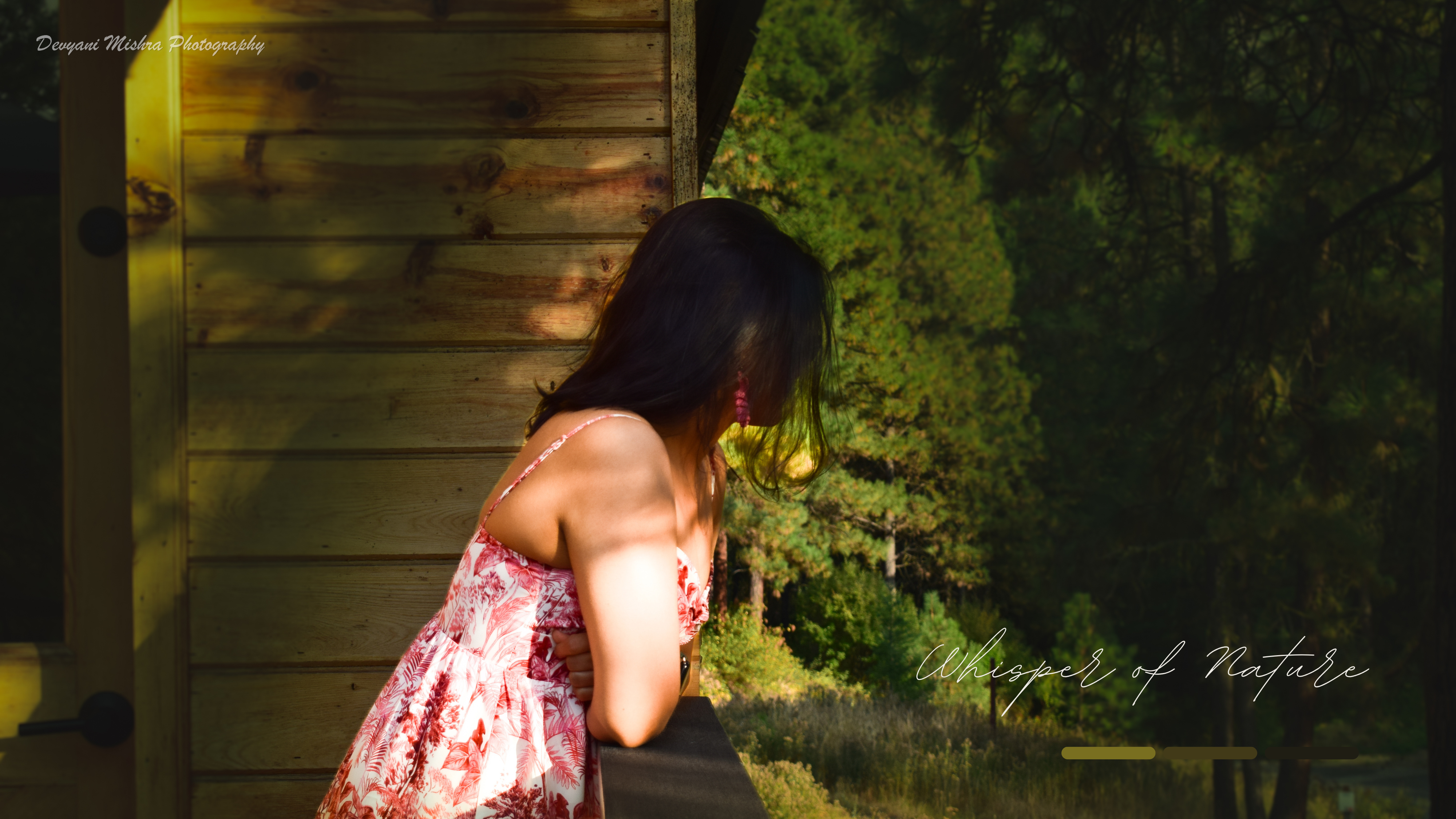 Woman in a floral sundress leaning over a cabin railing with an evergreen forest behind her